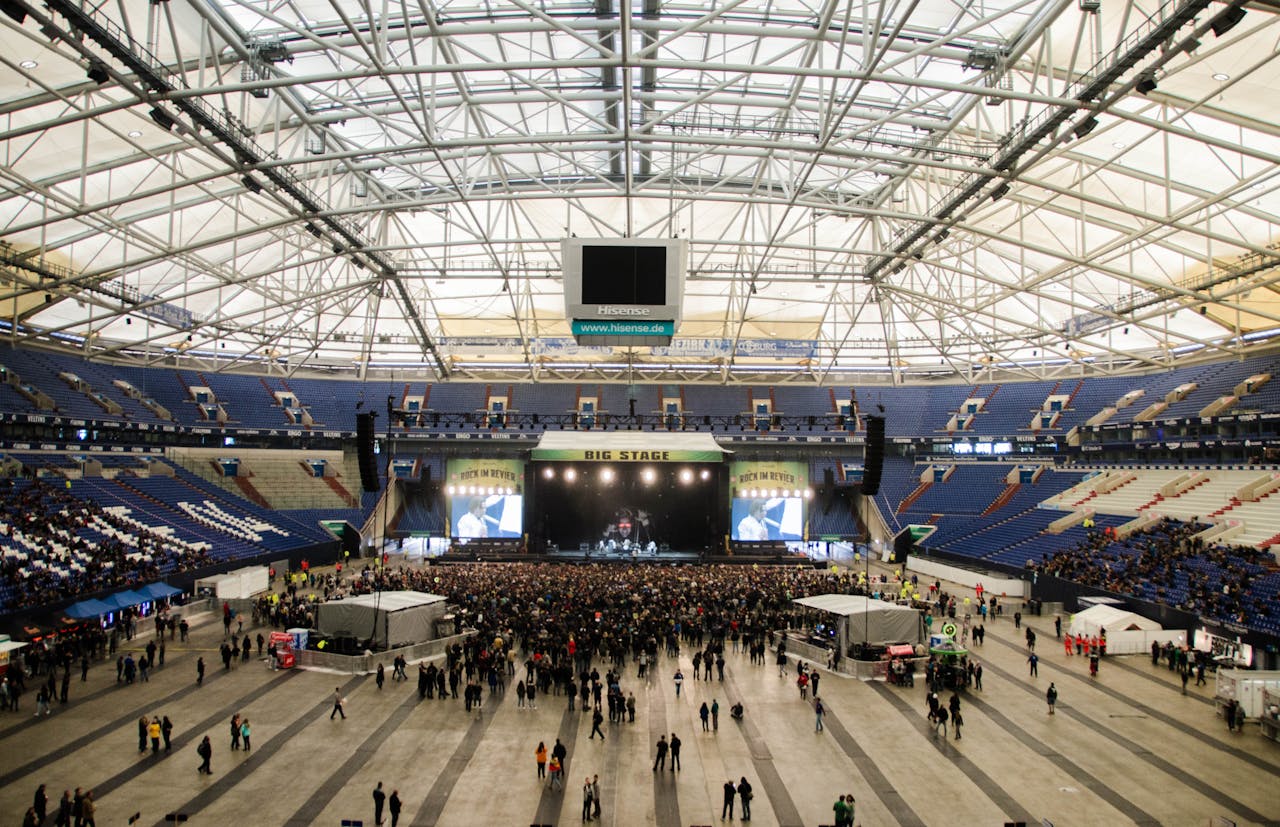 Wide shot of a crowded concert in a large indoor arena with a prominent stage.